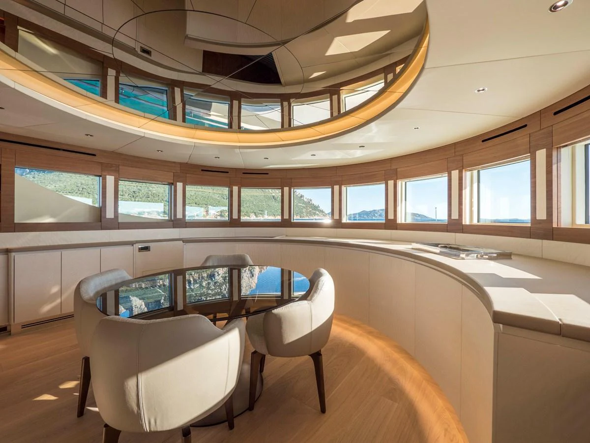 A luxurious yacht interior featuring a round table with chairs and panoramic windows offering stunning views. aboard MAXIMA Yacht for Sale