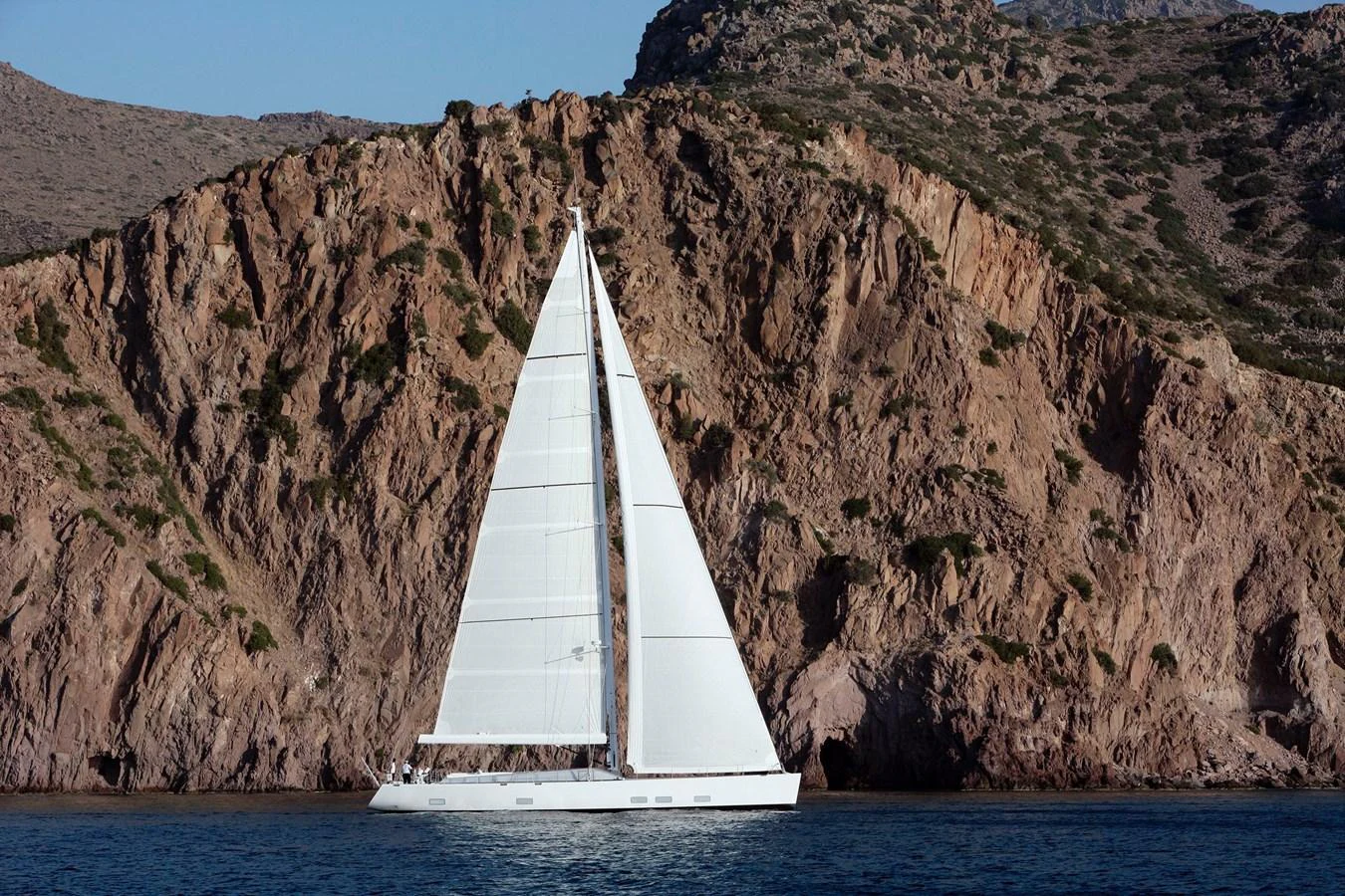 A sleek sailing yacht glides gracefully past rugged cliffs. aboard S/Y SENTINEL Yacht for Sale