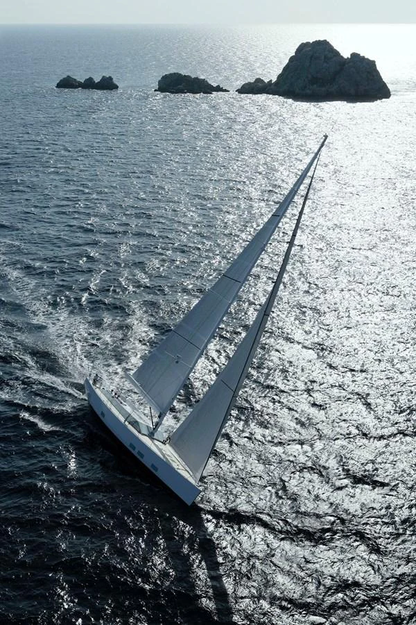 A sleek sailing yacht glides gracefully through the open sea near rocky formations. aboard S/Y SENTINEL Yacht for Sale