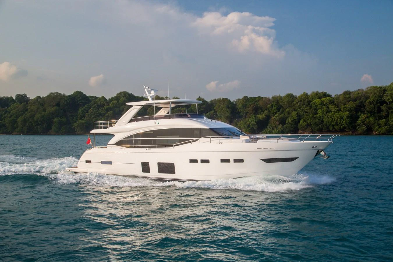 A sleek and modern yacht cruises through calm waters against a backdrop of lush greenery. aboard PRINCESS CHLOE Yacht for Sale