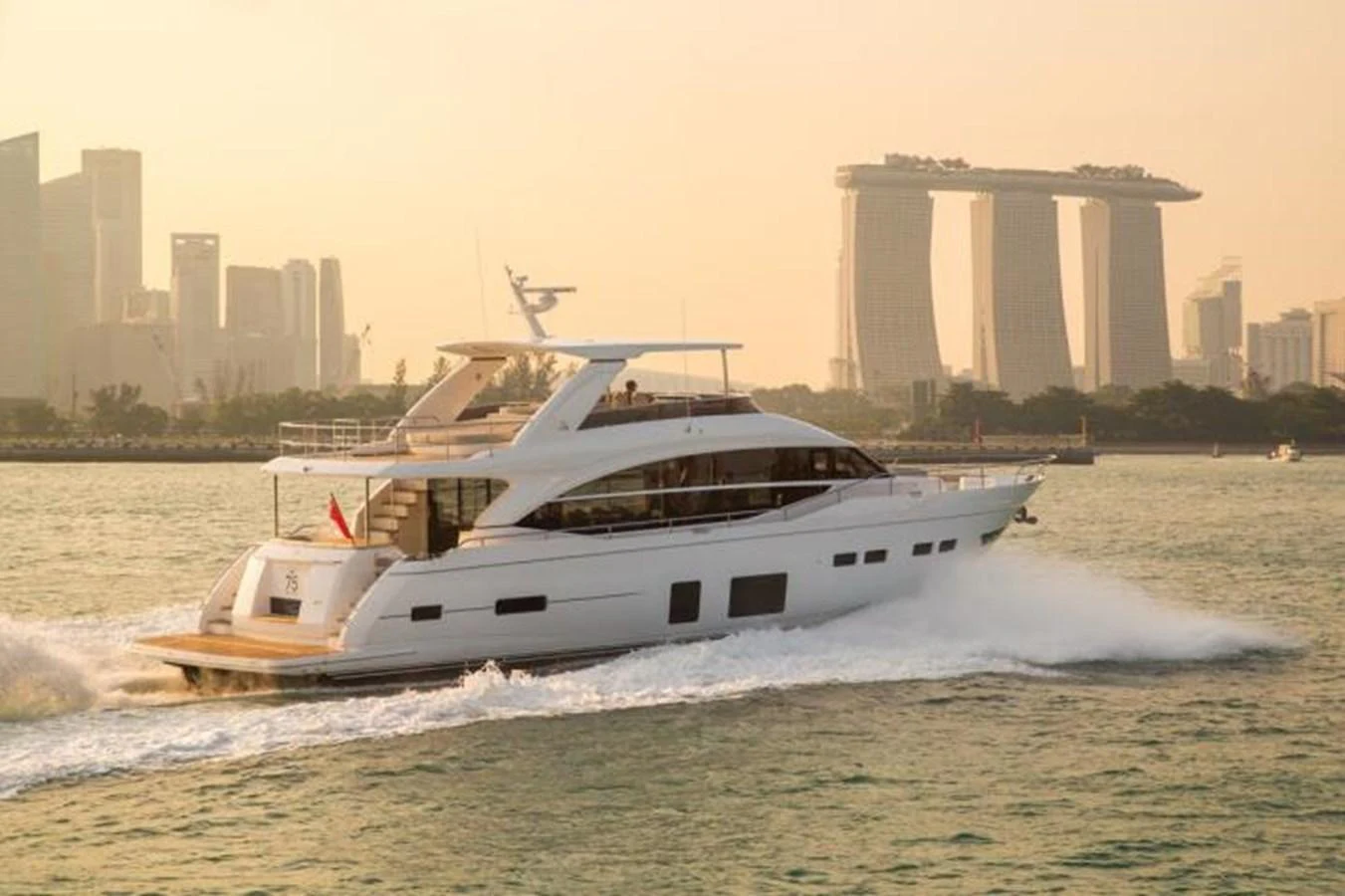 A sleek yacht cruises through calm waters with a city skyline in the background. aboard PRINCESS CHLOE Yacht for Sale
