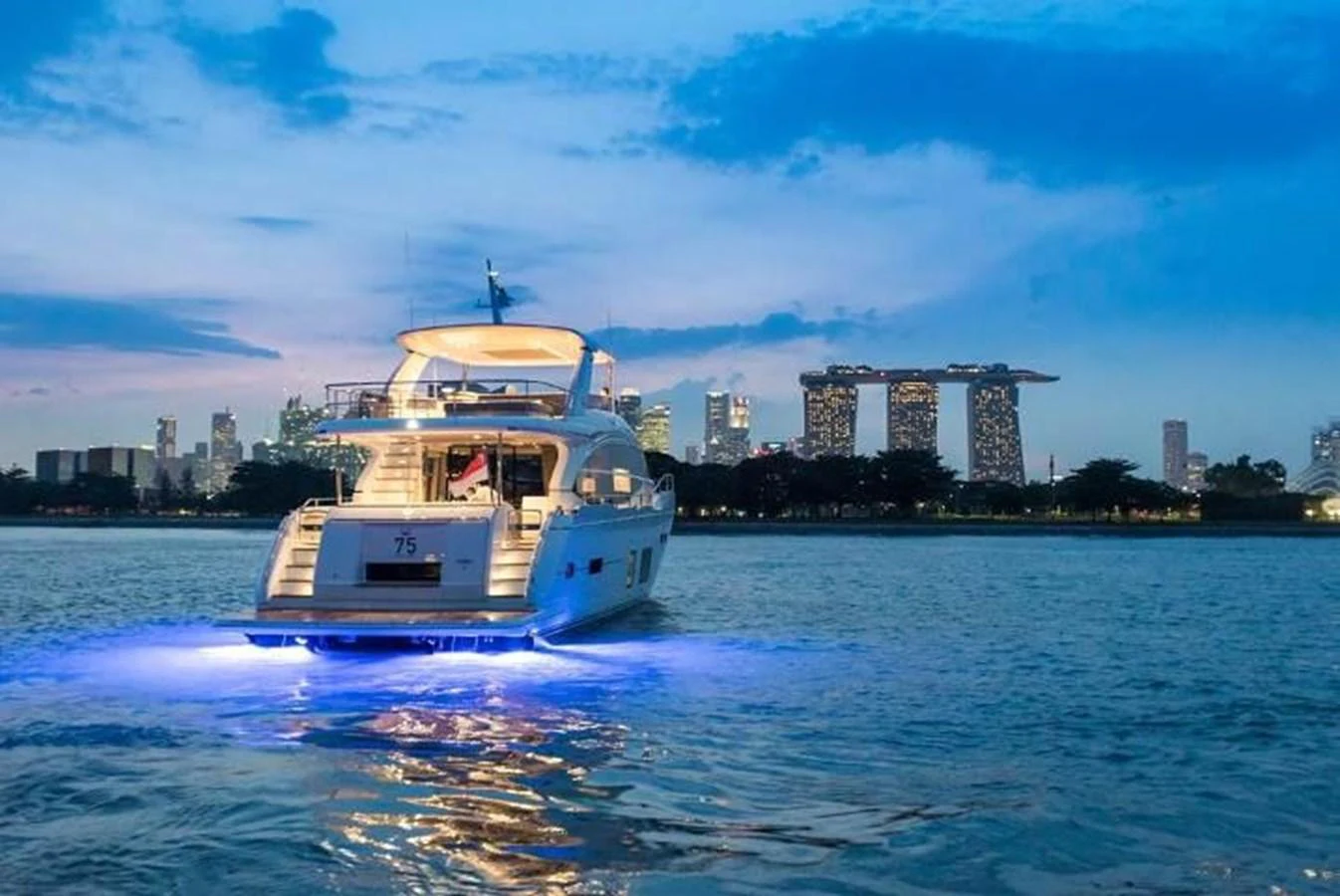 A luxurious yacht is illuminated against a stunning cityscape backdrop at dusk. aboard PRINCESS CHLOE Yacht for Sale