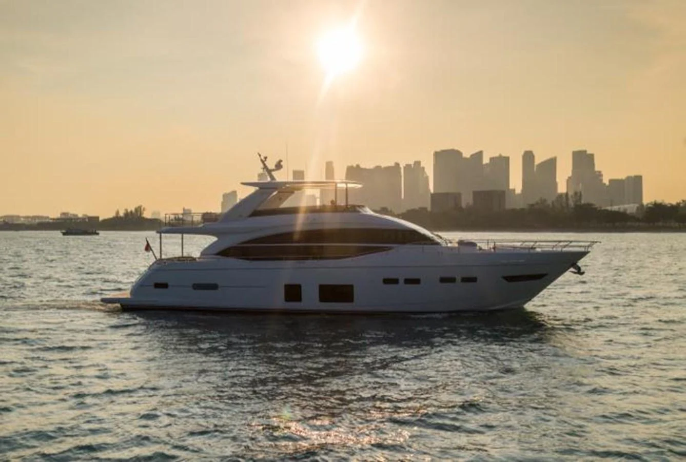 A sleek yacht cruises gracefully on the water with a city skyline in the background at sunset. aboard PRINCESS CHLOE Yacht for Sale
