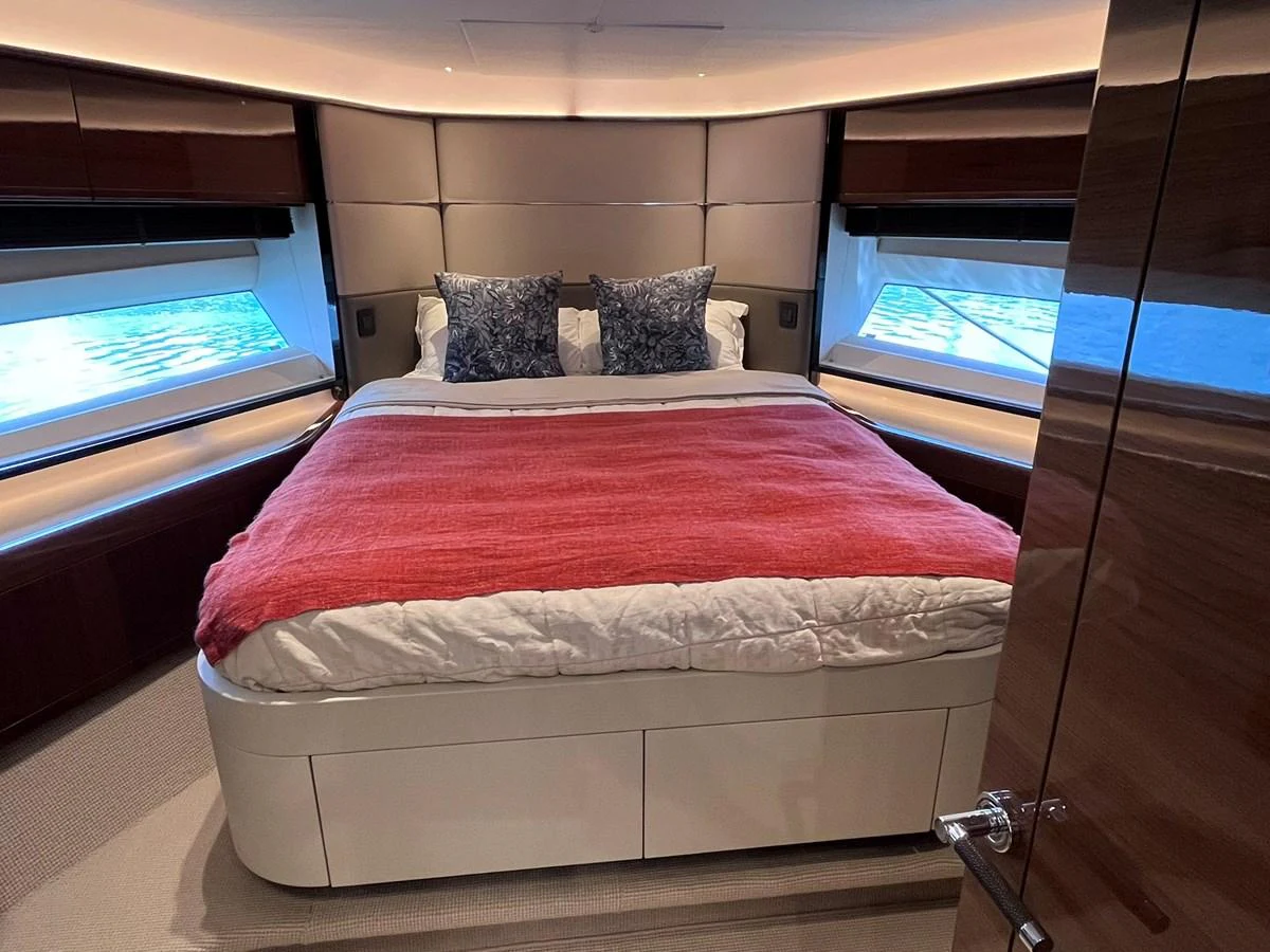 The stateroom features a plush bed with a vibrant red throw, flanked by large windows offering scenic views. aboard PRINCESS CHLOE Yacht for Sale