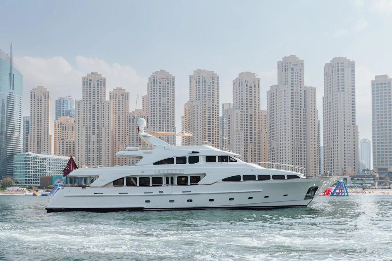 A sleek and elegant yacht cruises along the waterfront with a cityscape backdrop. aboard GALLUS Yacht for Sale