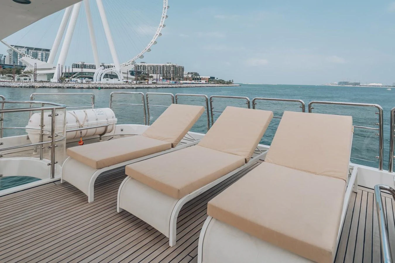 The sundeck features three comfortable lounge chairs with a stunning view of the water and a Ferris wheel in the background. aboard GALLUS Yacht for Sale