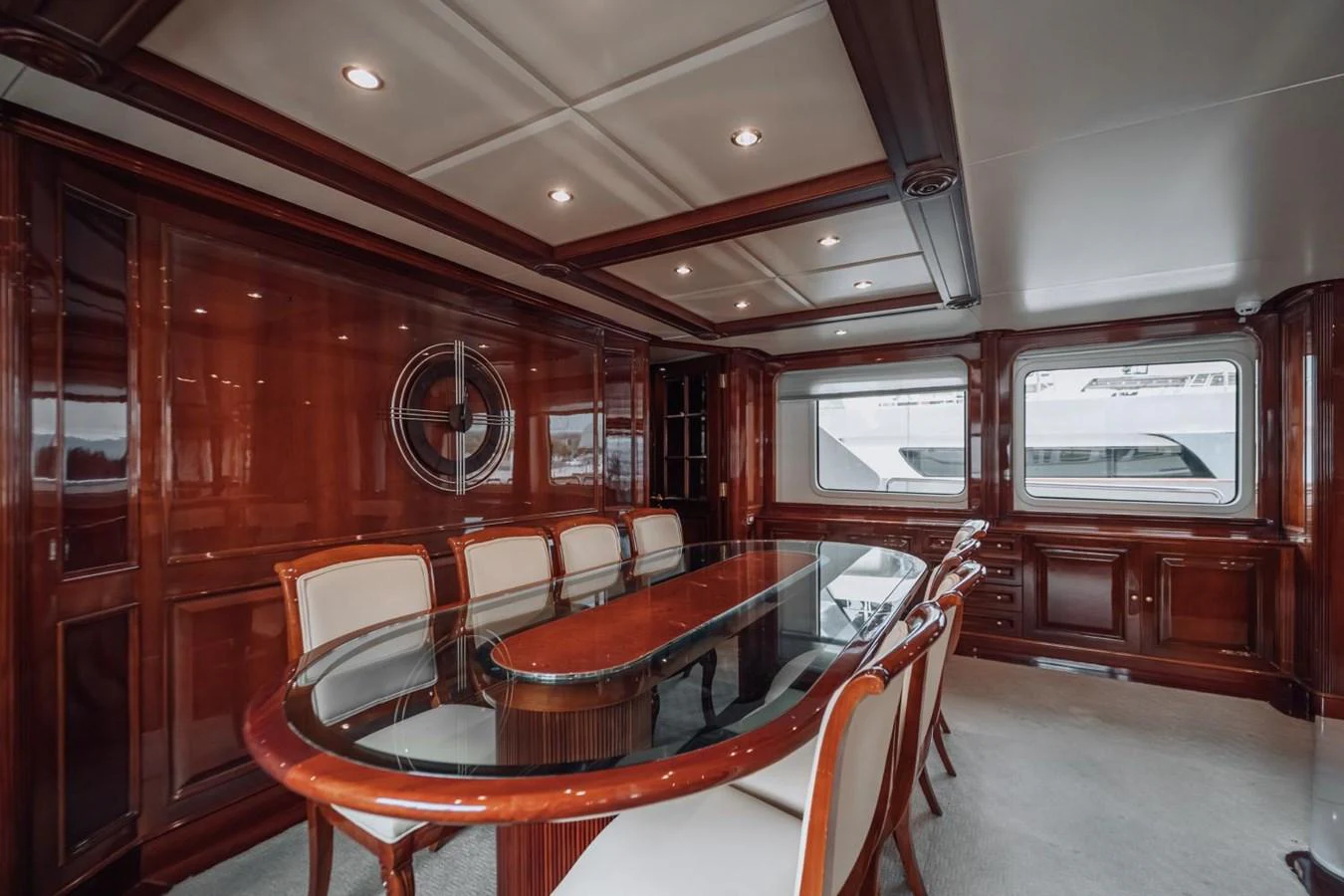 The yacht's dining area features elegant wood paneling and a large glass-top table surrounded by comfortable chairs. aboard GALLUS Yacht for Sale