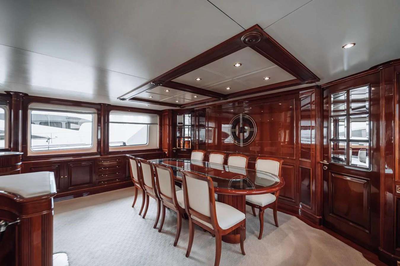 The yacht's dining area features elegant wooden paneling and a large glass-top table with upholstered chairs. aboard GALLUS Yacht for Sale