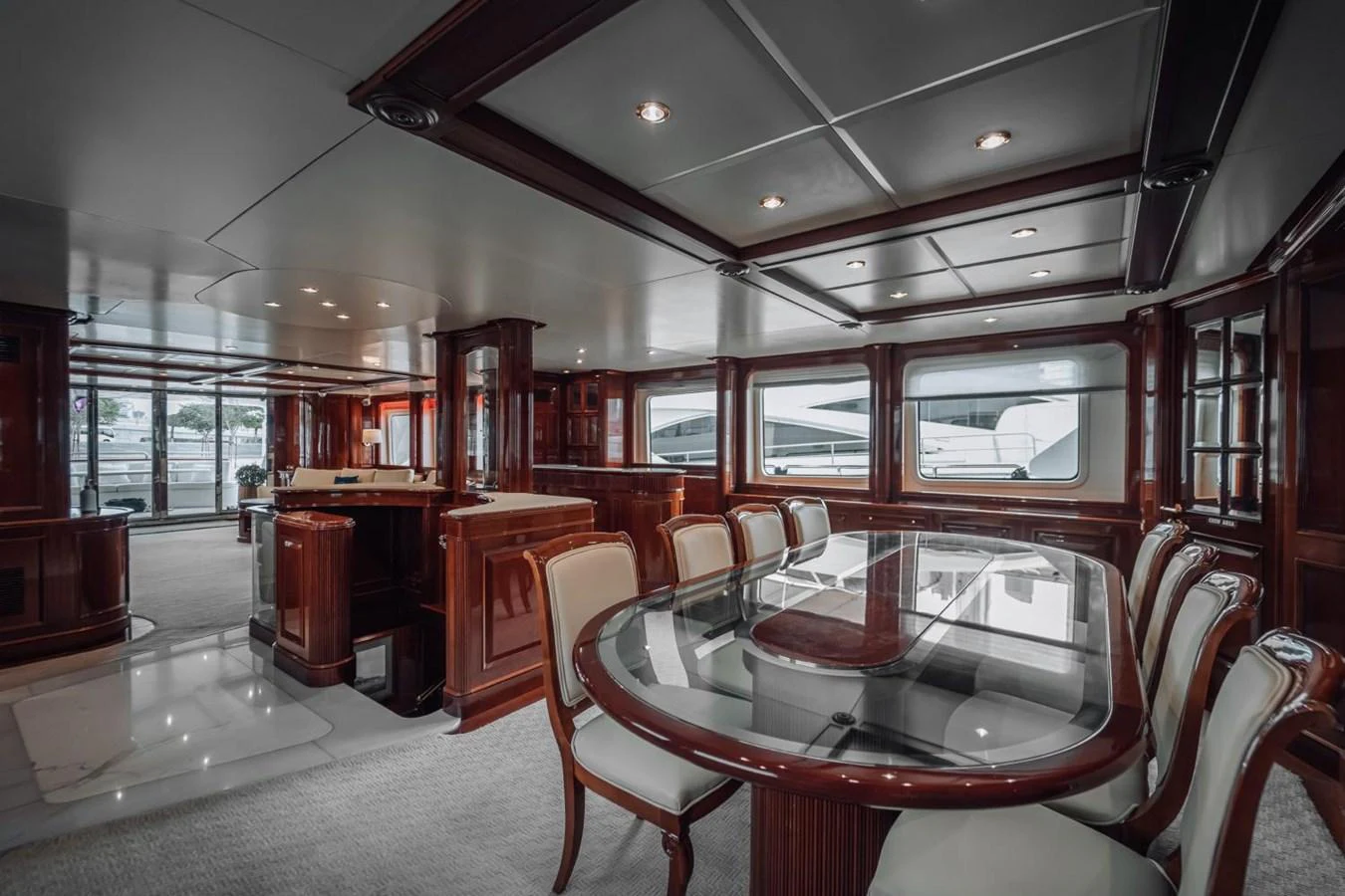 The yacht's dining area features elegant wood paneling and a large glass-top table surrounded by plush chairs. aboard GALLUS Yacht for Sale