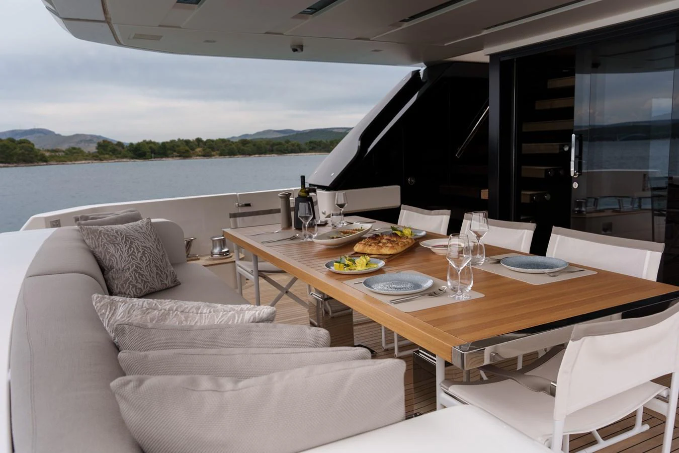 The aft deck features a stylish dining area with a wooden table set for a meal, surrounded by comfortable seating and offering scenic views. aboard DESTINO Yacht for Sale