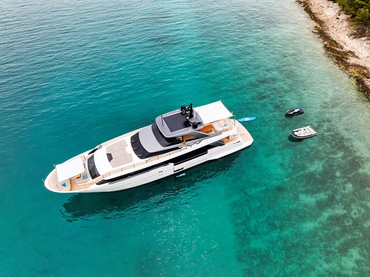 A sleek and modern yacht glides gracefully on turquoise waters near a rocky shoreline. aboard DESTINO Yacht for Sale