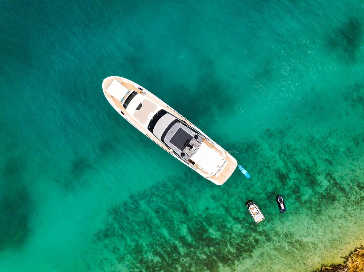 An aerial view of a sleek yacht anchored in clear turquoise waters, accompanied by a few small watercraft. aboard DESTINO Yacht for Sale