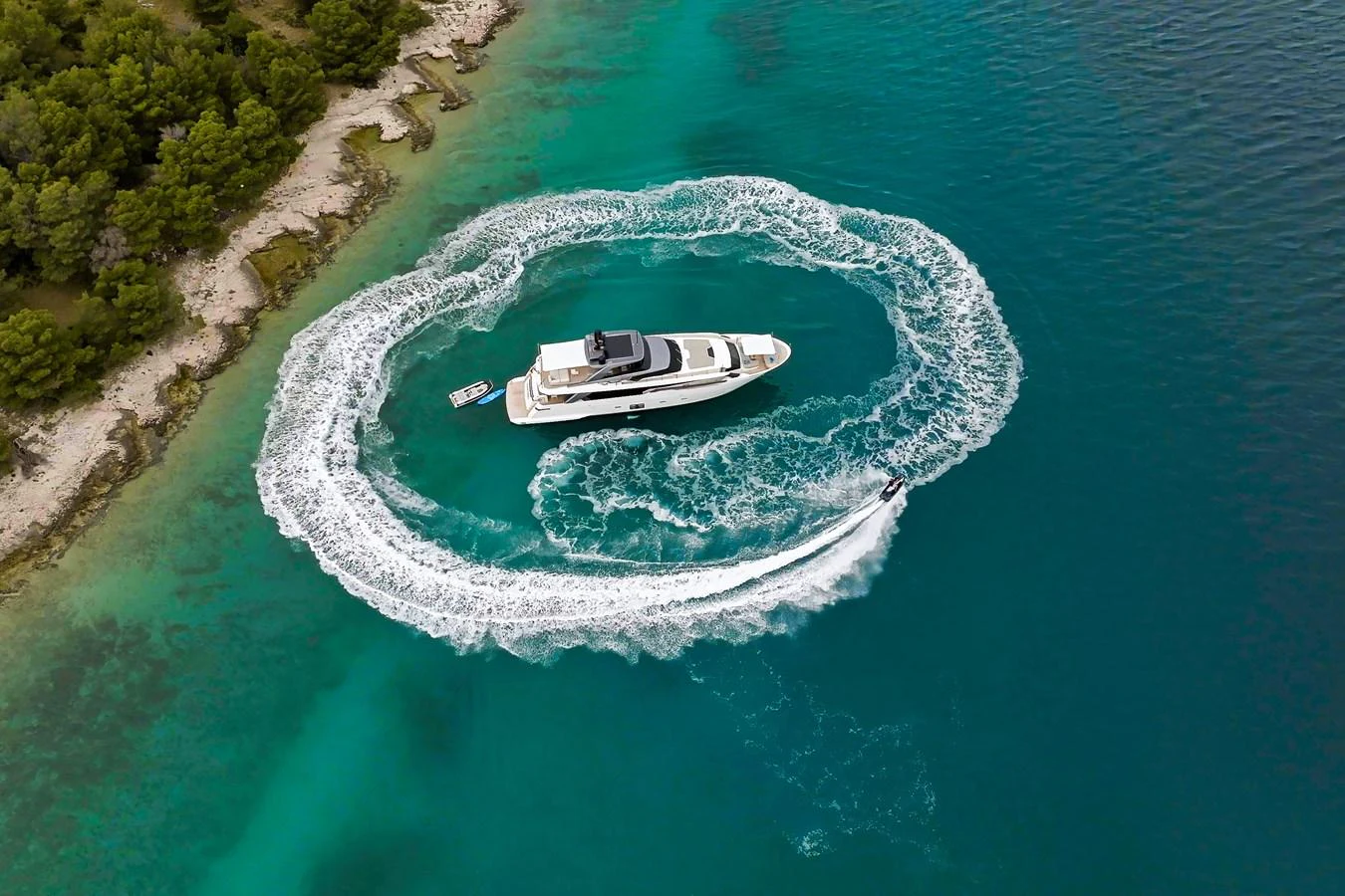 A luxurious yacht is anchored in clear turquoise waters, surrounded by a wake from a nearby watercraft. aboard DESTINO Yacht for Sale