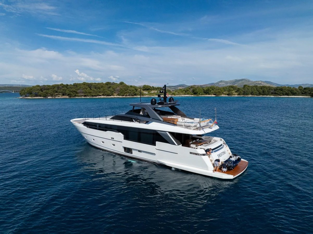 A sleek and modern yacht cruising on calm blue waters with a scenic island backdrop. aboard DESTINO Yacht for Sale