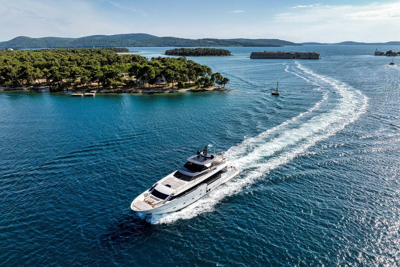 A sleek yacht cruises through pristine blue waters near a lush, green island. aboard DESTINO Yacht for Sale