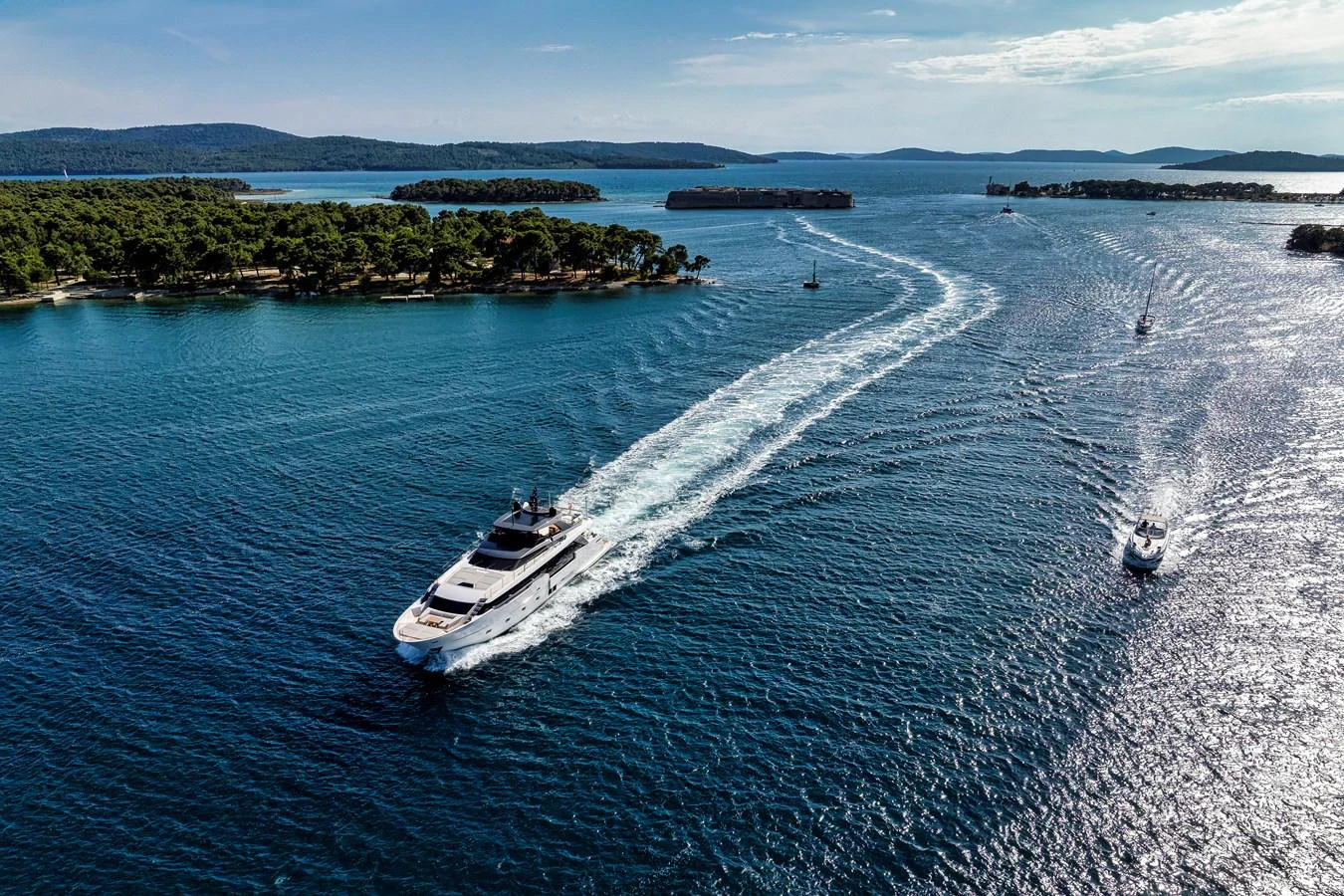 A sleek yacht cruises through a serene, island-dotted seascape under a clear sky. aboard DESTINO Yacht for Sale