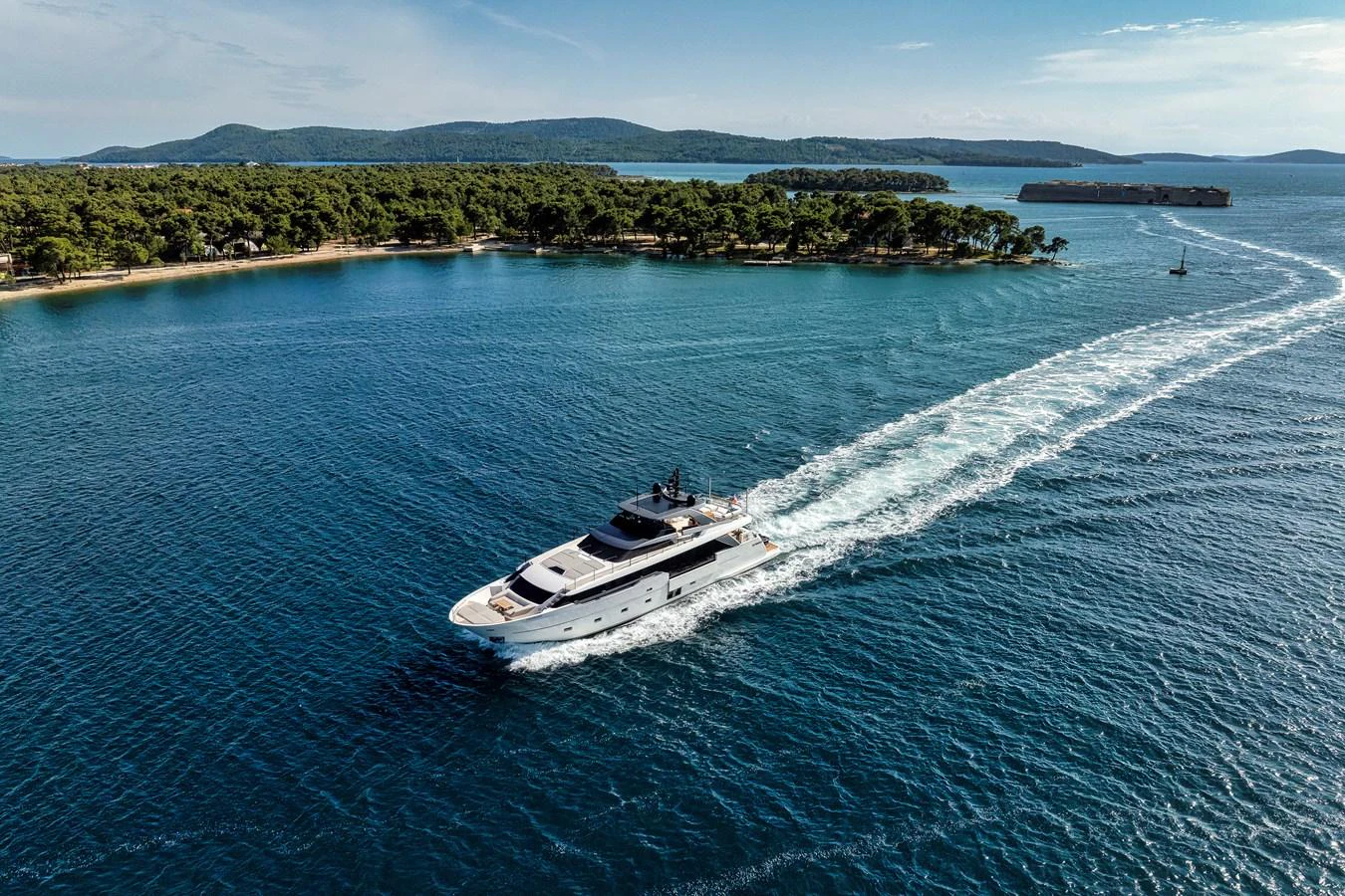 A sleek yacht cruises through serene blue waters near a lush, green island. aboard DESTINO Yacht for Sale