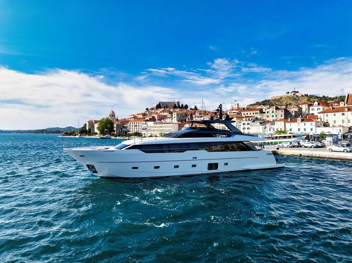 A sleek and modern yacht cruising near a picturesque coastal town under a clear blue sky. aboard DESTINO Yacht for Sale