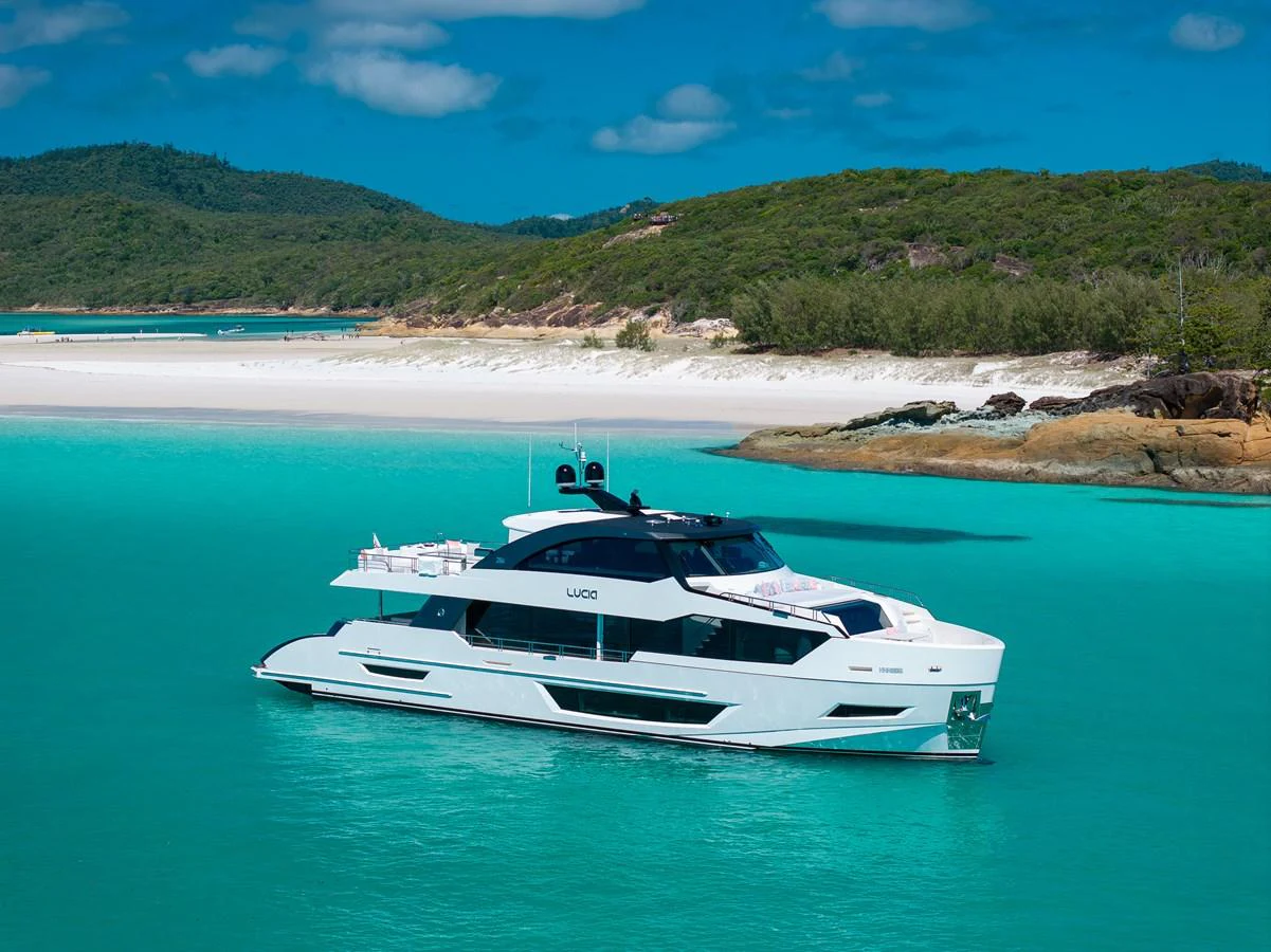 A sleek yacht cruises through turquoise waters near a picturesque beach and lush greenery. aboard G Yacht for Sale