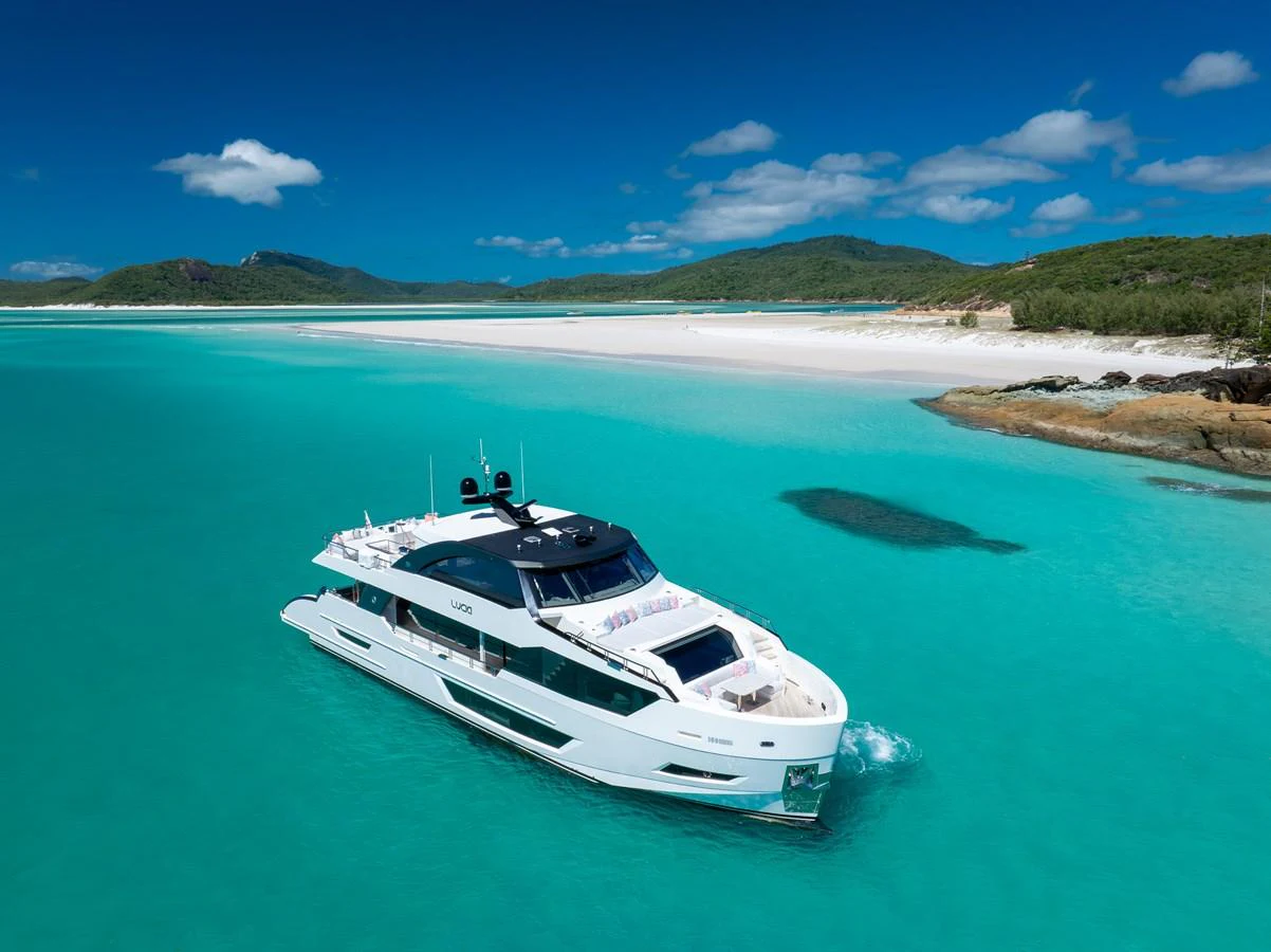A sleek yacht cruises through turquoise waters near a pristine beach. aboard G Yacht for Sale