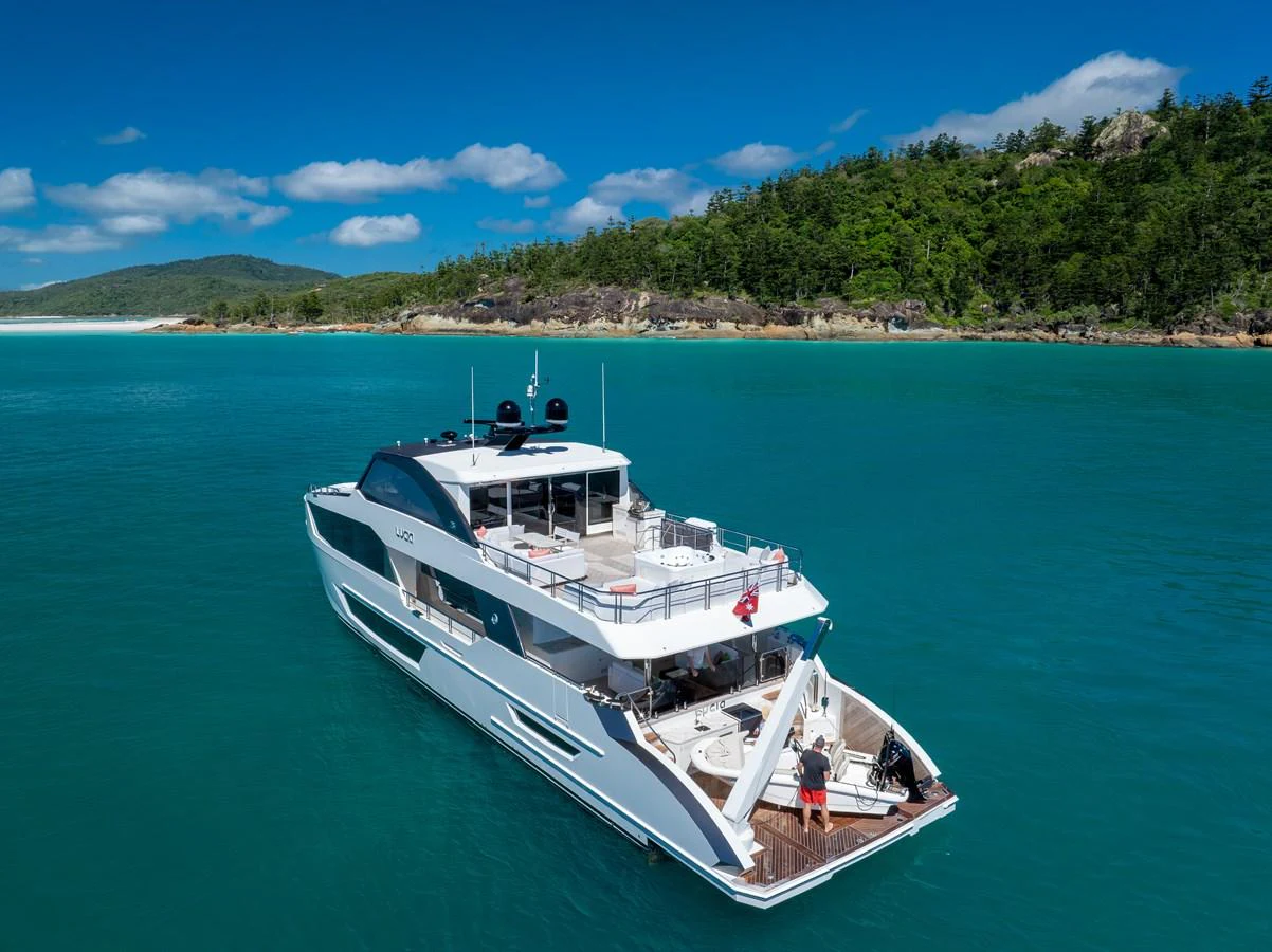 A sleek yacht cruises in clear turquoise waters near a lush, green coastline. aboard G Yacht for Sale