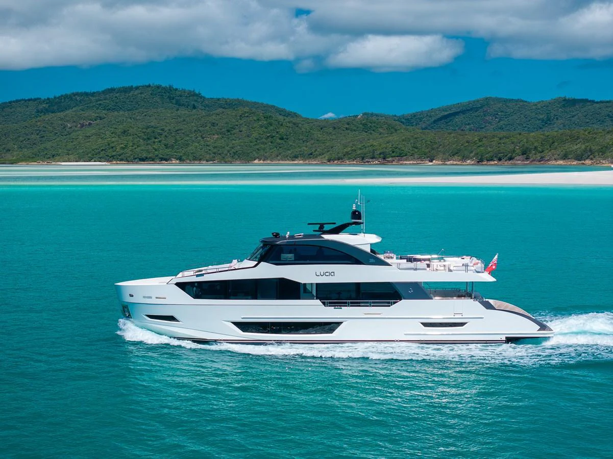 A sleek yacht cruises through turquoise waters against a backdrop of lush green hills. aboard G Yacht for Sale