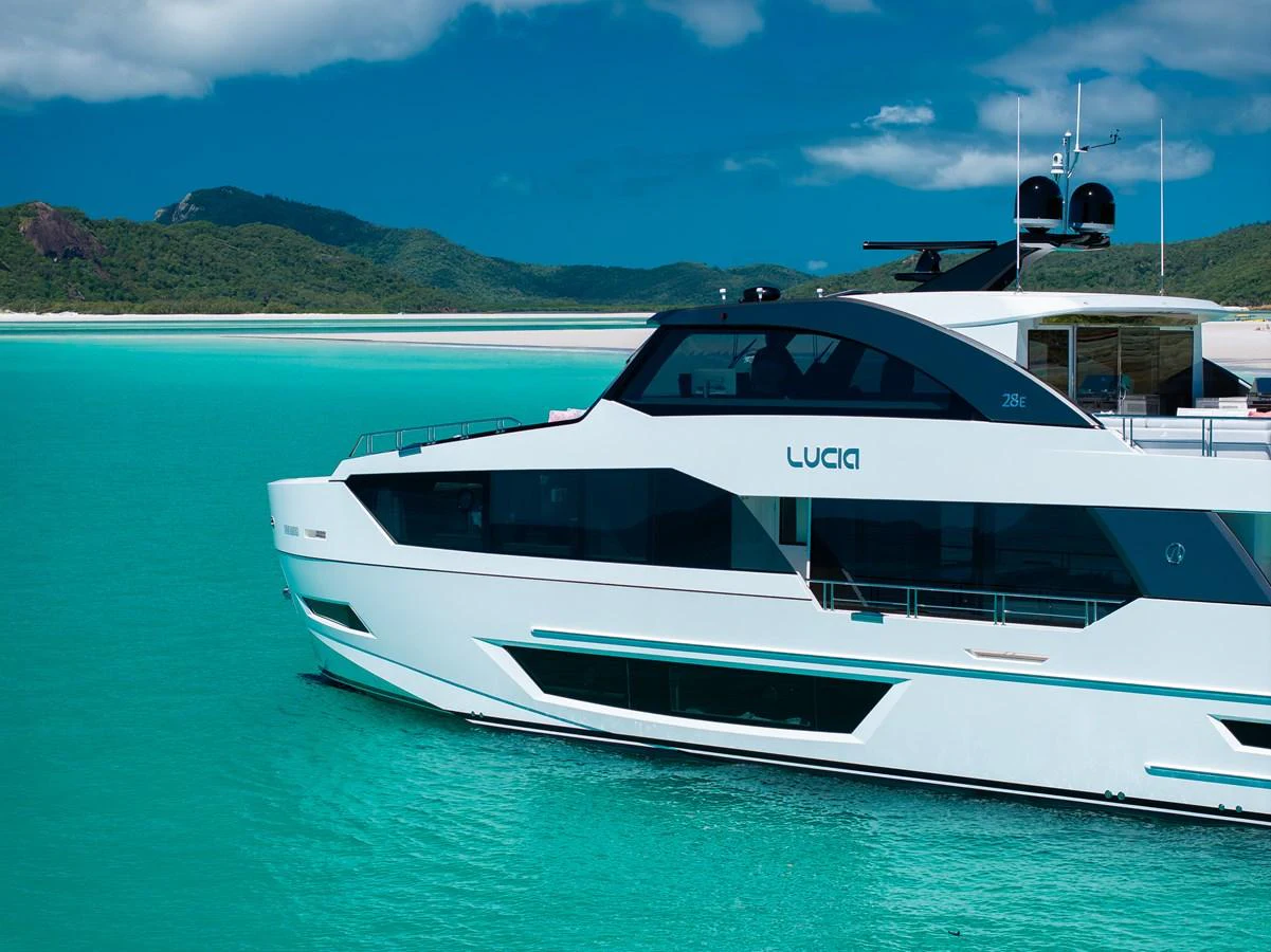 A sleek yacht glides through turquoise waters against a backdrop of lush hills and a clear sky. aboard G Yacht for Sale