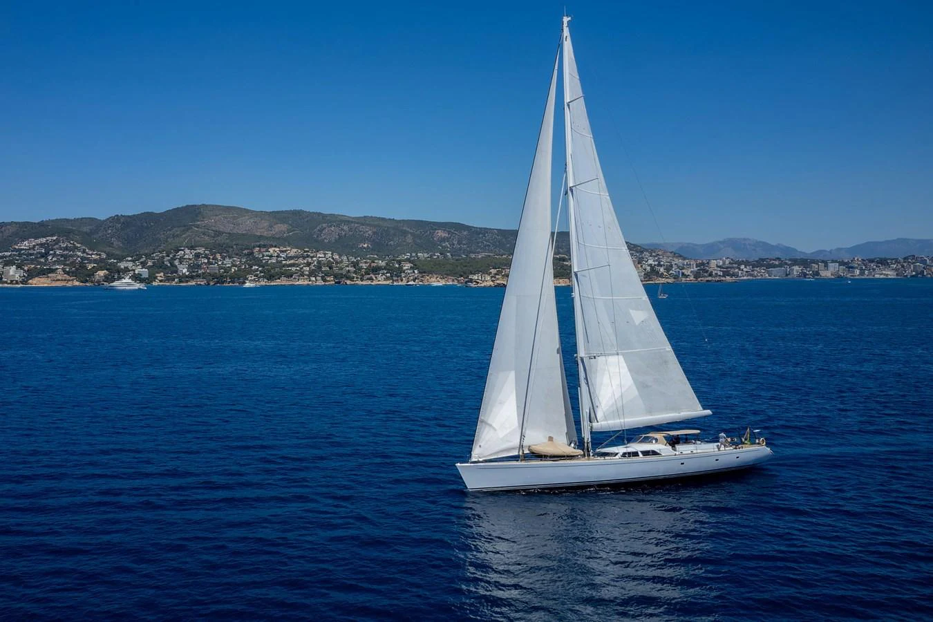 A sleek sailing yacht glides gracefully on calm blue waters with picturesque coastal scenery in the background. aboard EPIPHANY Yacht for Sale