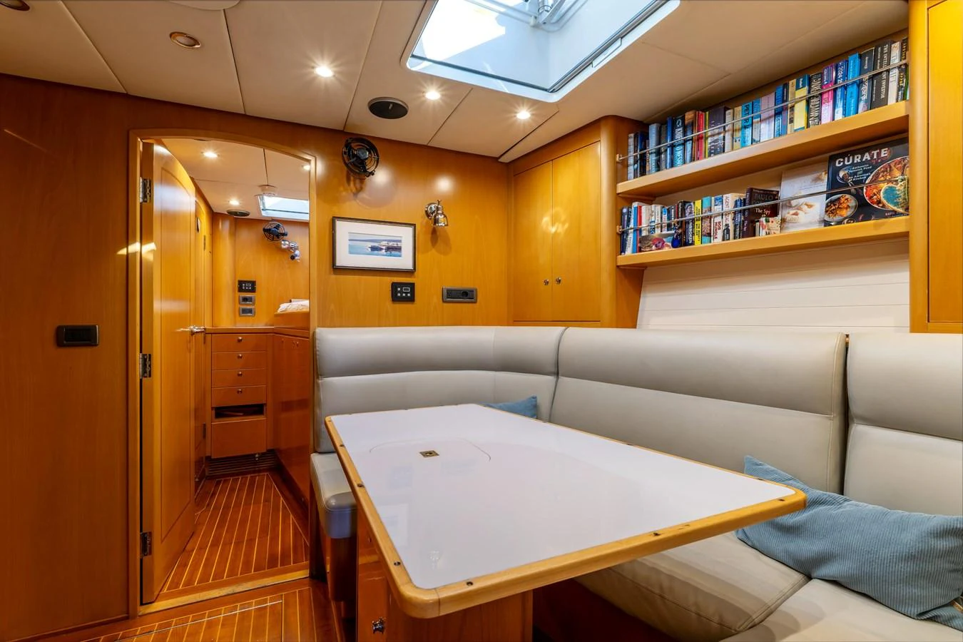 The cozy saloon features a comfortable seating area with a table, surrounded by warm wooden cabinetry and a skylight above. aboard EPIPHANY Yacht for Sale