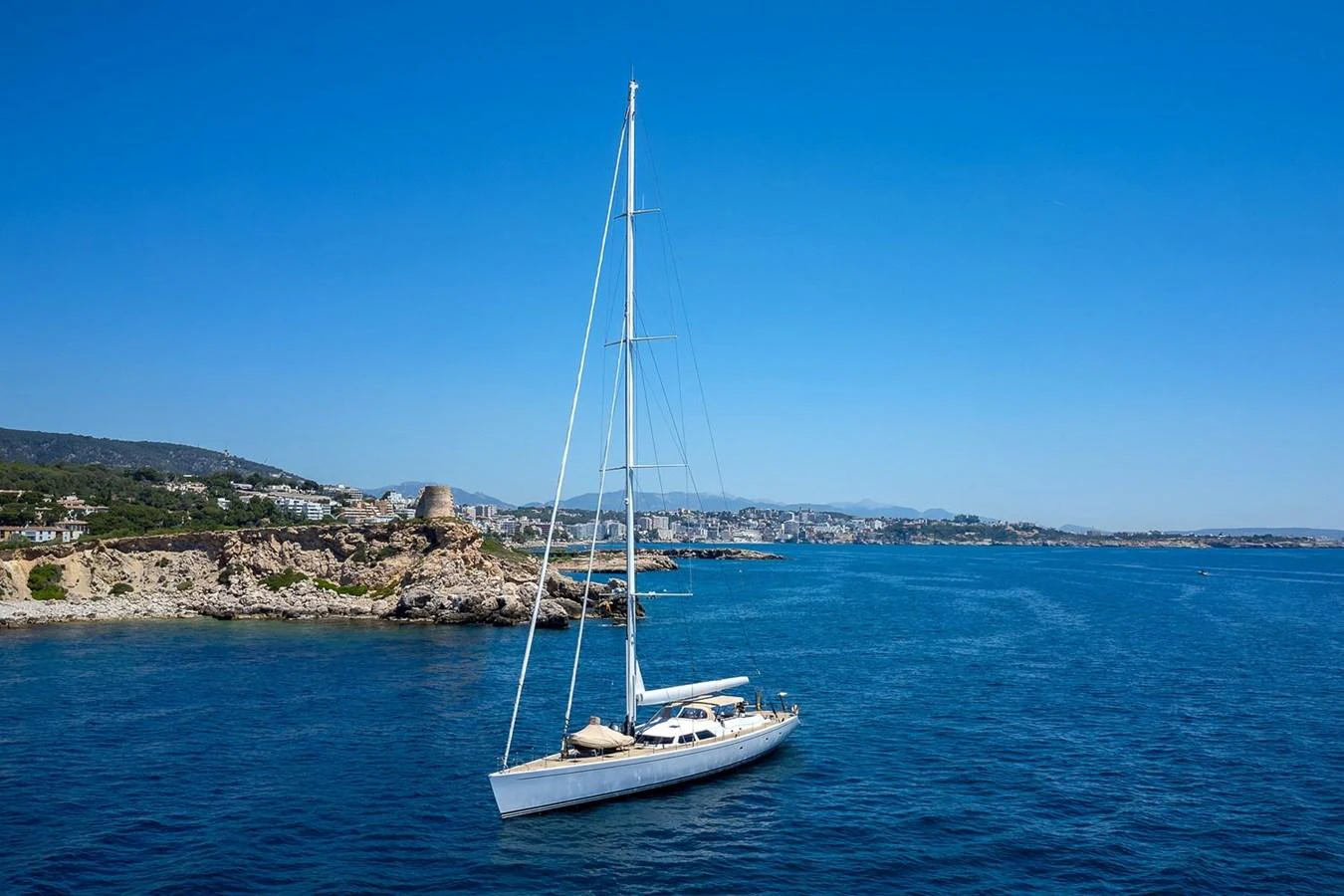 A sleek sailing yacht glides gracefully on calm blue waters with a picturesque coastline in the background. aboard EPIPHANY Yacht for Sale