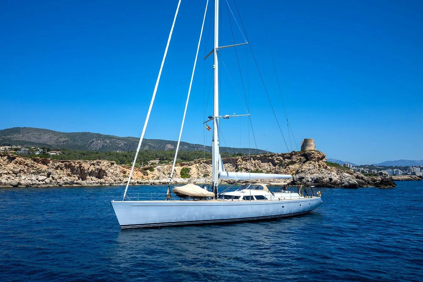 A sleek sailing yacht glides gracefully on calm blue waters with a scenic coastal backdrop. aboard EPIPHANY Yacht for Sale
