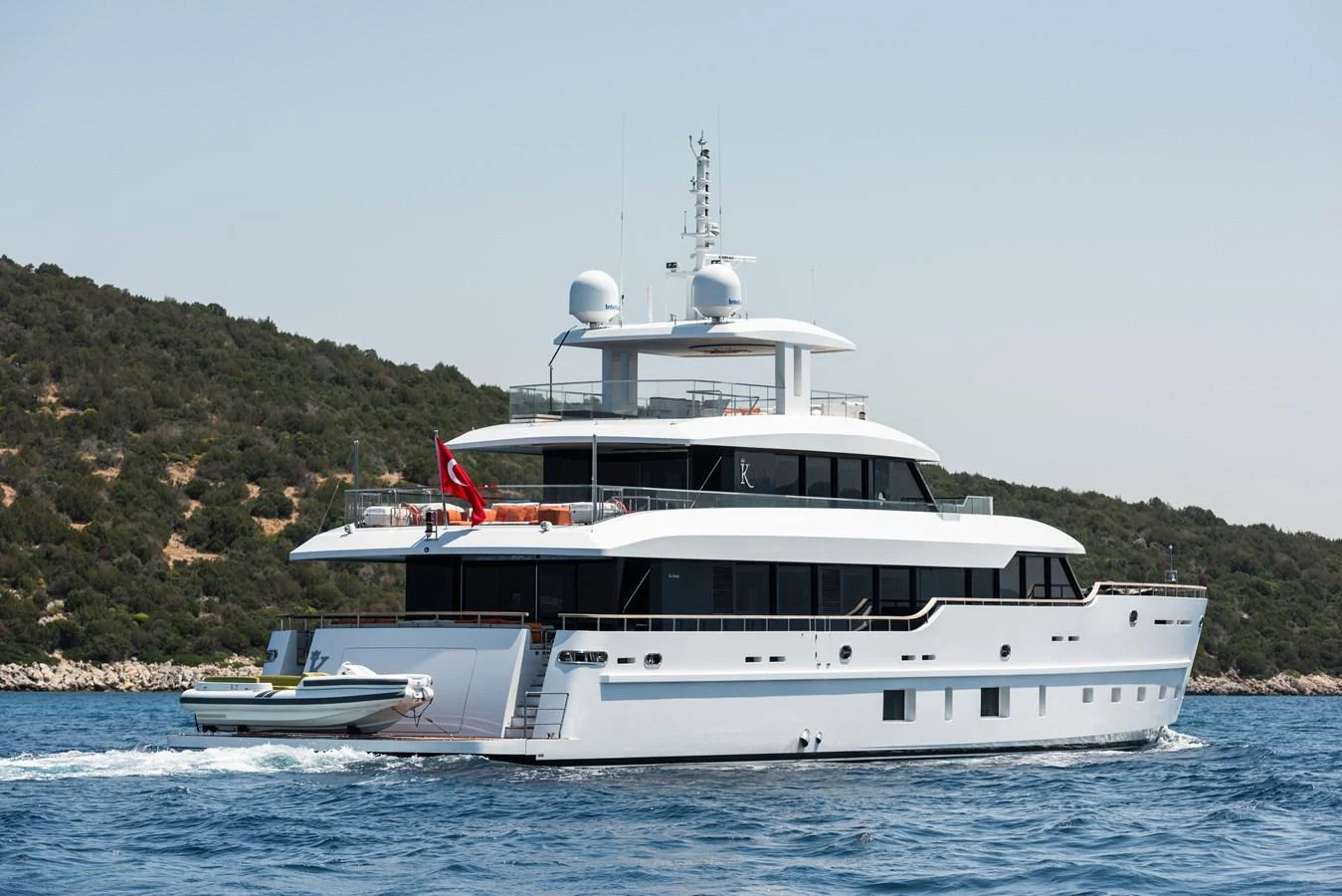 A sleek and modern yacht cruising on calm waters with a scenic coastline in the background. aboard K Yacht for Sale