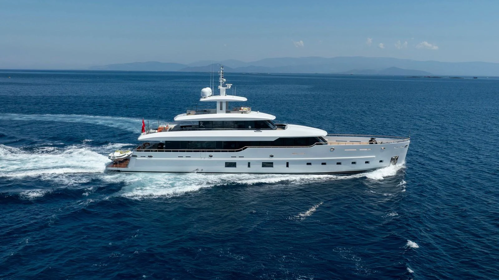 A sleek and modern yacht cruising through clear blue waters on a sunny day. aboard K Yacht for Sale