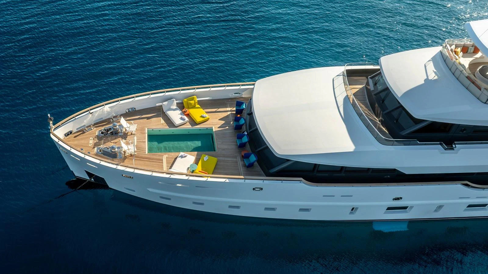 A luxurious yacht with a spacious deck featuring a pool and sun loungers, cruising on clear blue waters. aboard K Yacht for Sale
