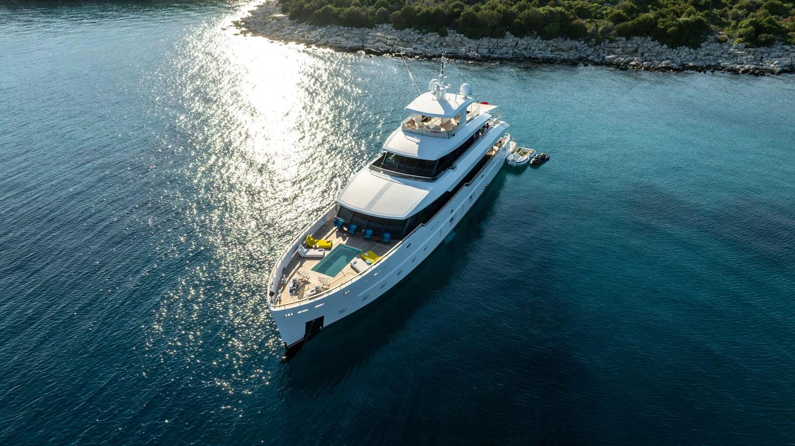 A luxurious yacht glides gracefully on serene blue waters near a rocky shoreline. aboard K Yacht for Sale