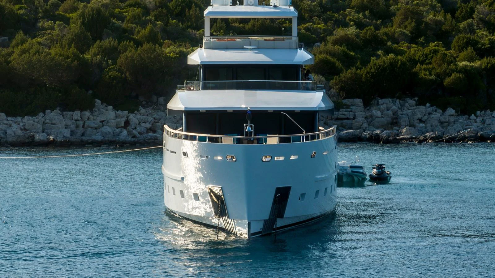 A sleek yacht is anchored in a serene bay with lush greenery in the background. aboard K Yacht for Sale