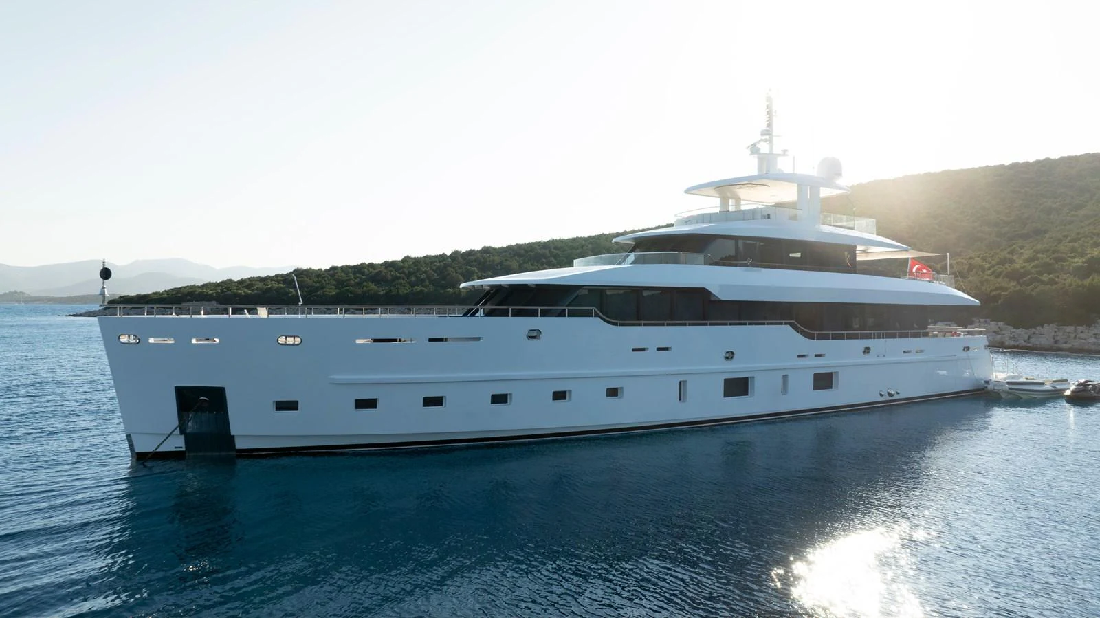 A sleek and modern yacht is anchored in a serene coastal area, bathed in sunlight. aboard K Yacht for Sale