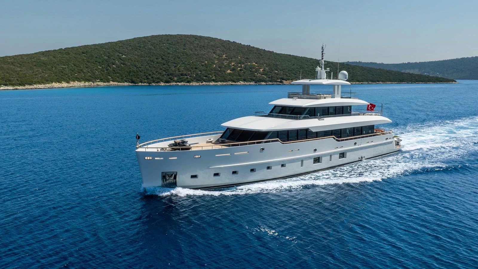 A sleek yacht cruises through clear blue waters with a scenic island backdrop. aboard K Yacht for Sale