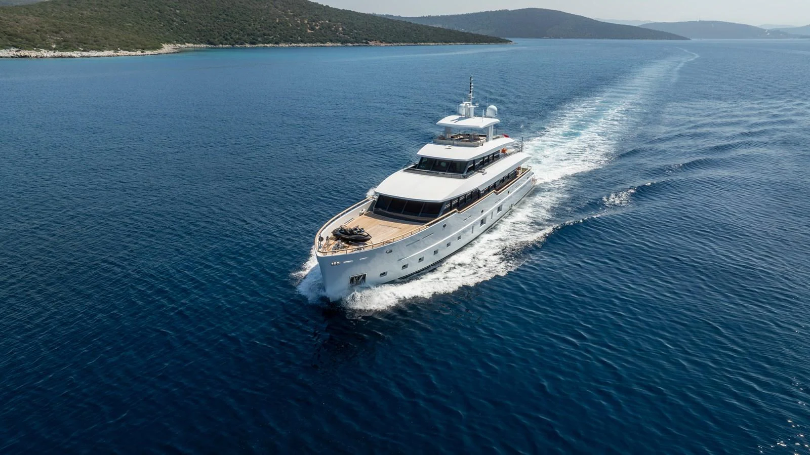 A sleek yacht glides through calm, blue waters with a scenic coastline in the background. aboard K Yacht for Sale