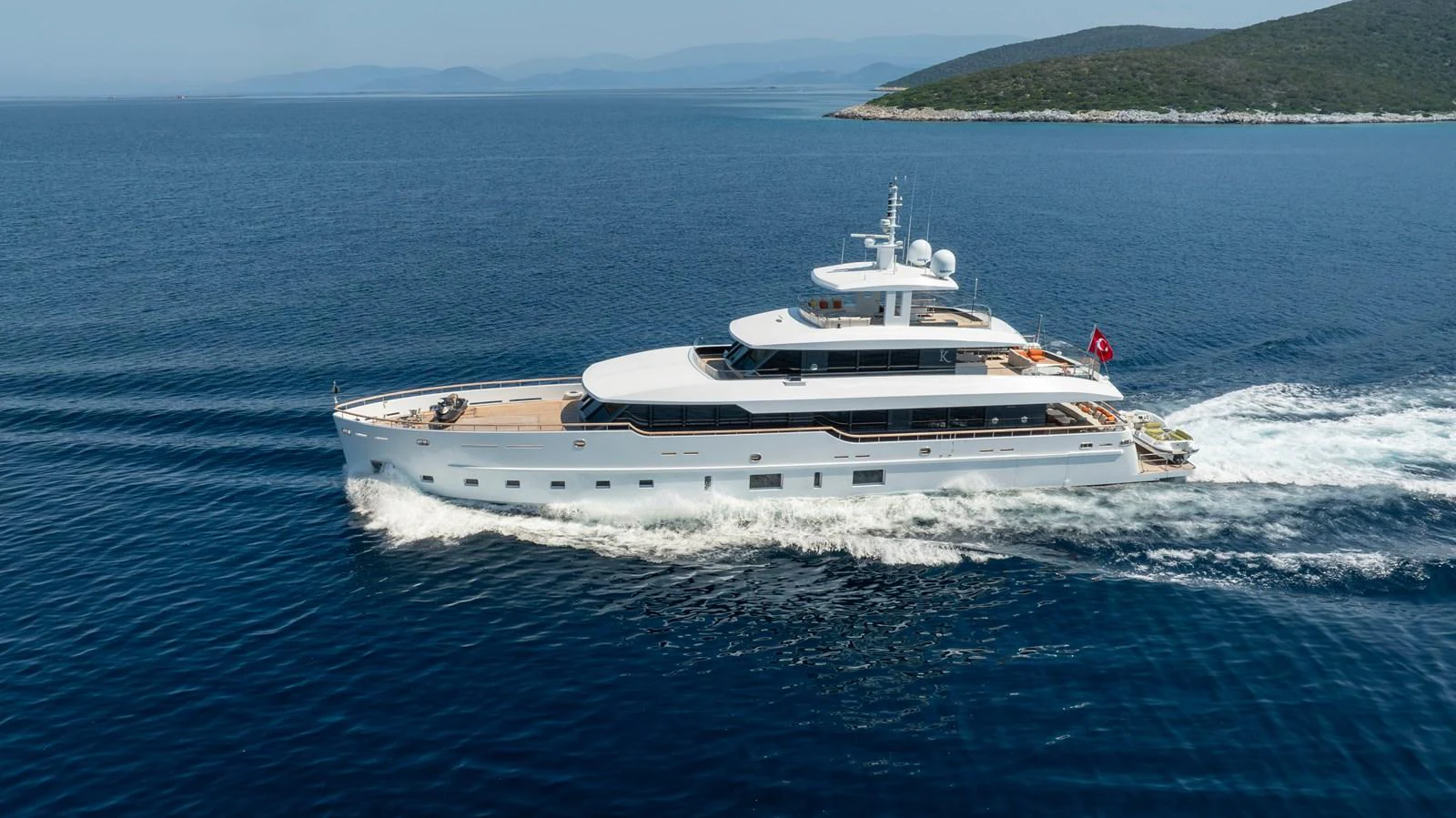 A sleek and modern yacht cruises through calm blue waters near a scenic coastline. aboard K Yacht for Sale