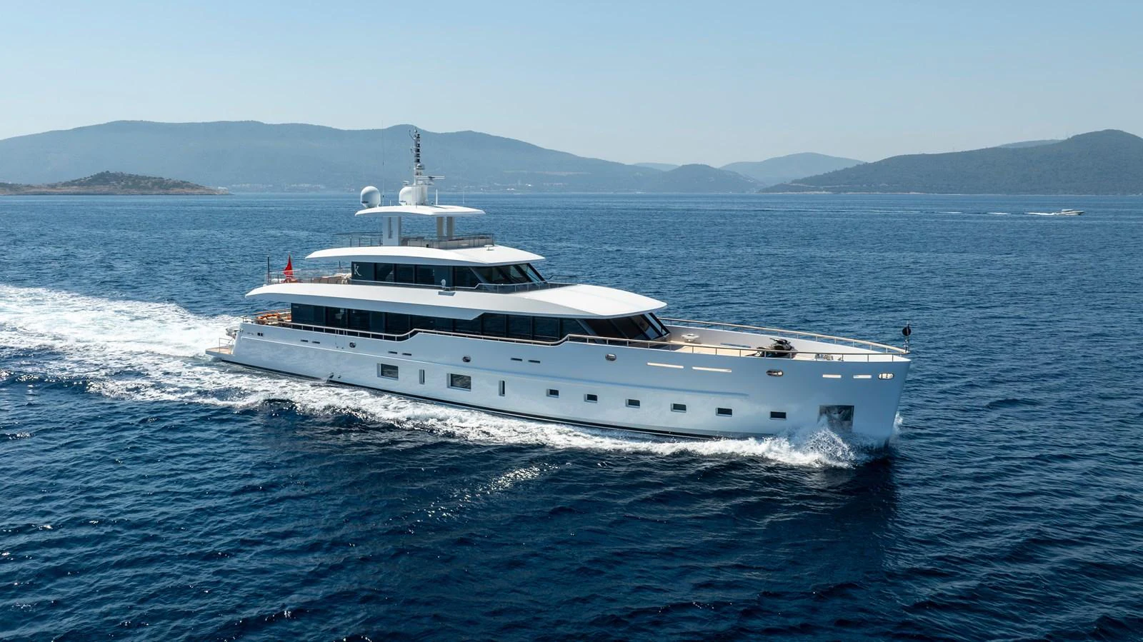A sleek and modern yacht cruises through calm blue waters with scenic hills in the background. aboard K Yacht for Sale