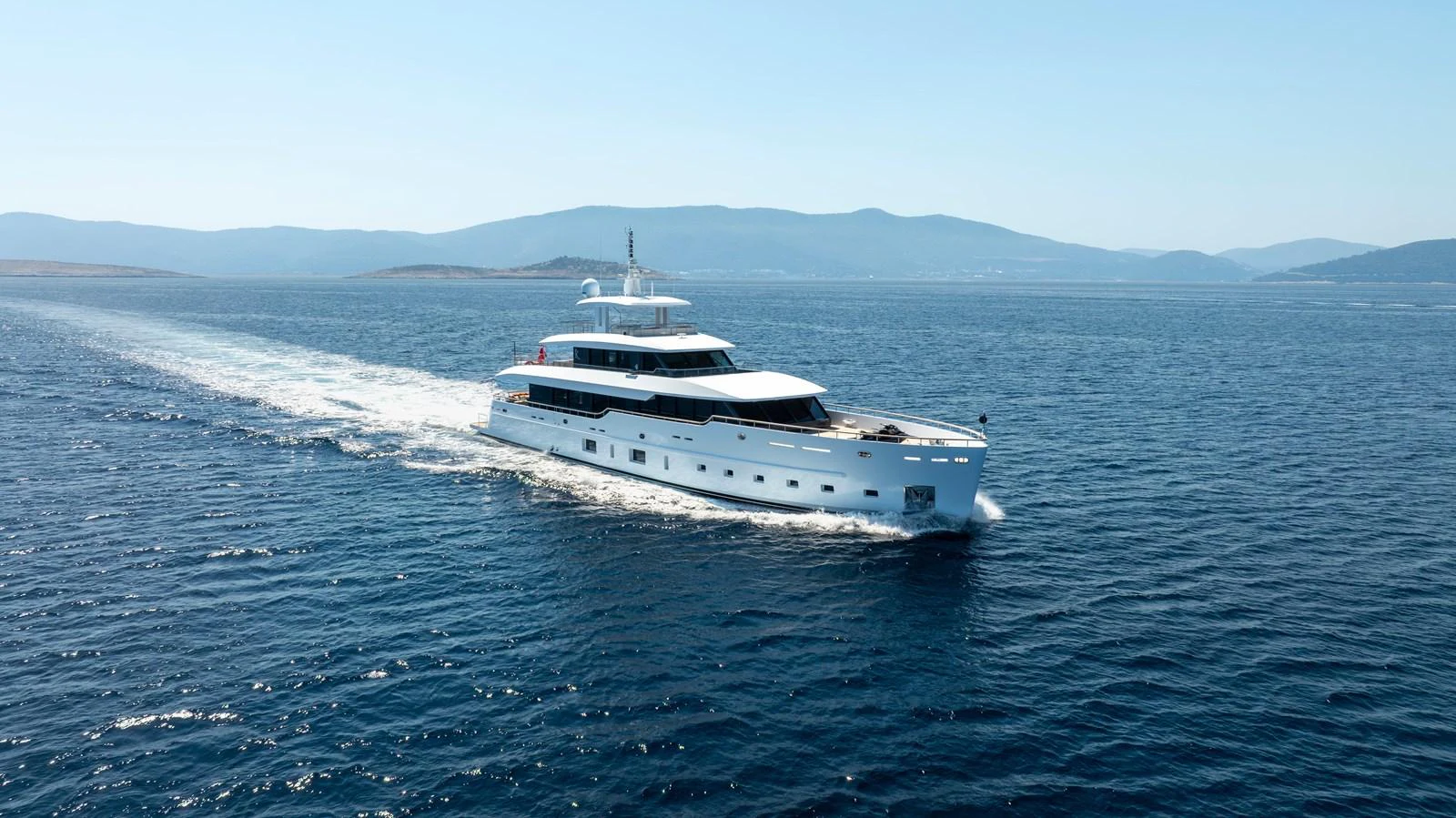 A sleek white yacht cruises through calm blue waters with scenic hills in the background. aboard K Yacht for Sale
