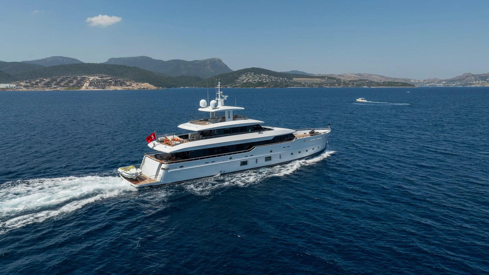 A luxurious yacht cruises through clear blue waters with scenic hills in the background. aboard K Yacht for Sale