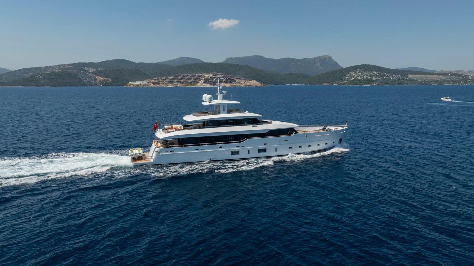 A sleek and modern yacht cruises through calm blue waters with scenic hills in the background. aboard K Yacht for Sale