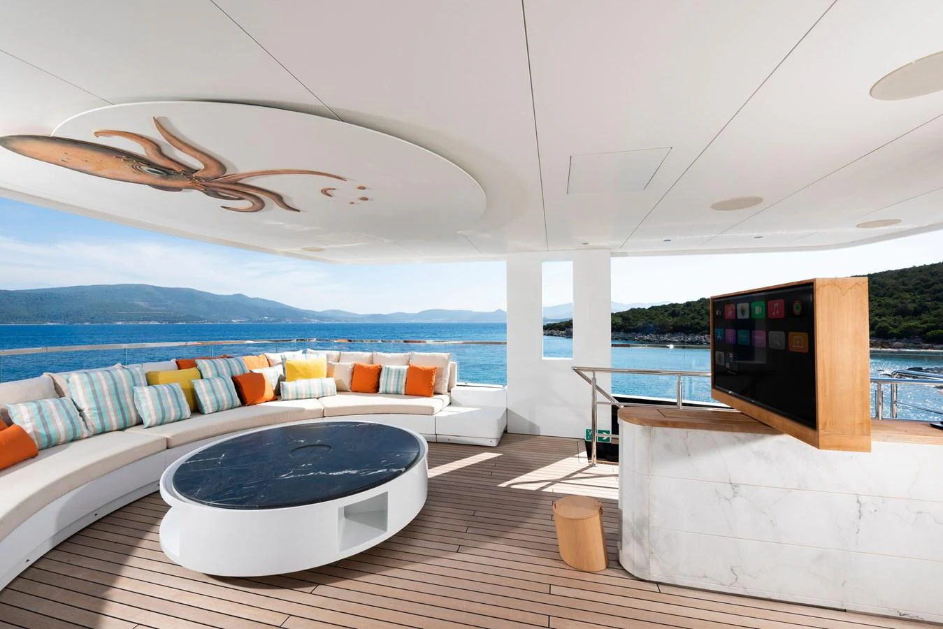The aft deck features a stylish seating area with a round table and a pop-up TV, offering stunning views of the surrounding waters. aboard K Yacht for Sale