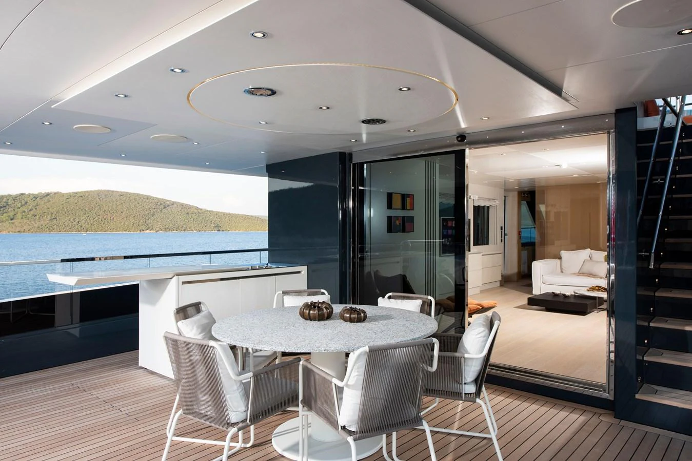 The aft deck features a stylish dining area with a round table and comfortable seating, seamlessly transitioning into a luxurious interior lounge. aboard K Yacht for Sale