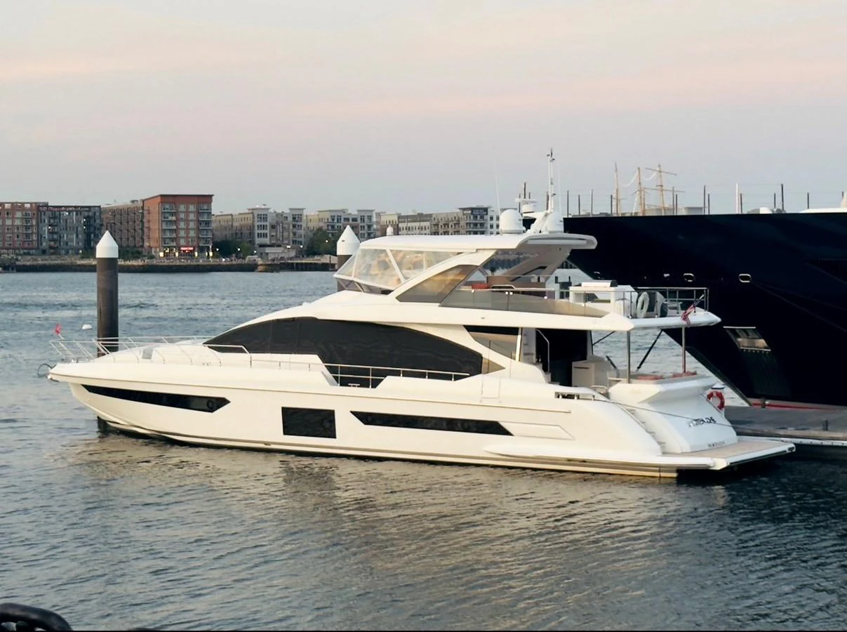 A sleek, modern yacht docked at a marina with a cityscape in the background. aboard 2022 AZIMUT GRANDE 25M Yacht for Sale