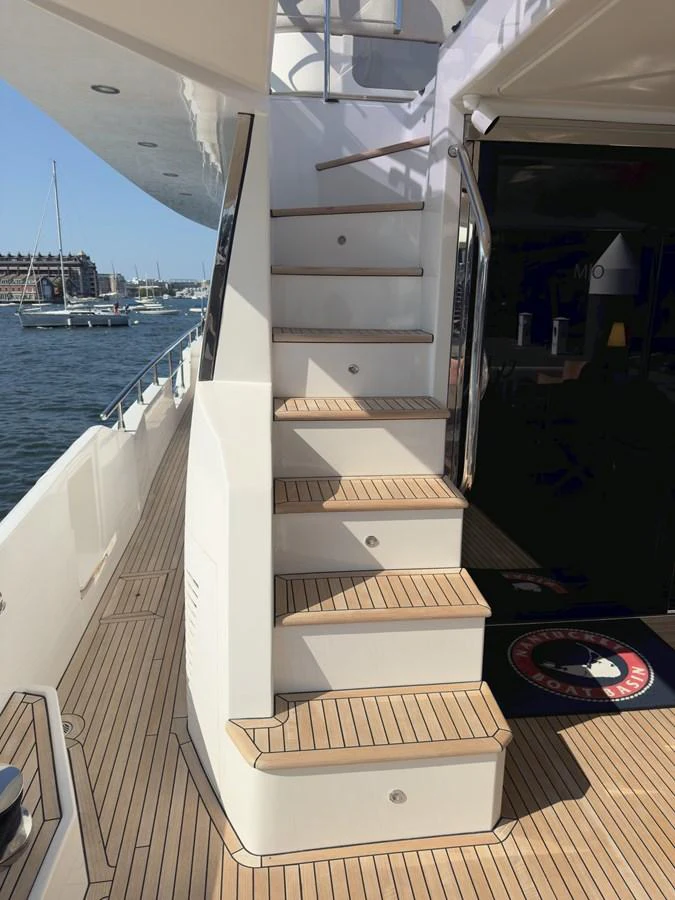 The image showcases a side deck with a staircase leading to the upper deck, featuring teak flooring and a view of the marina. aboard 2022 AZIMUT GRANDE 25M Yacht for Sale