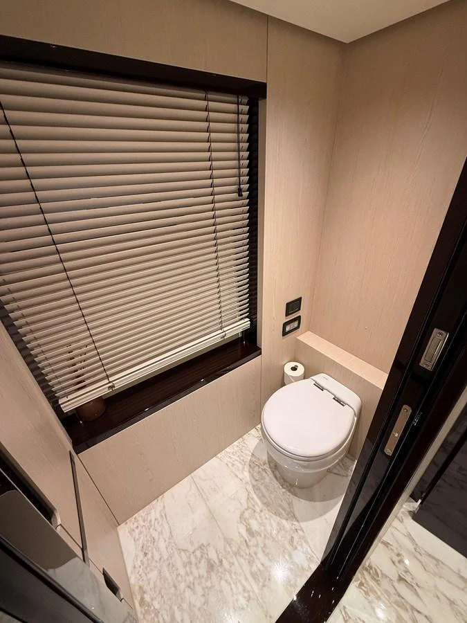 A sleek and modern yacht bathroom with marble flooring and a window with blinds. aboard 2022 AZIMUT GRANDE 25M Yacht for Sale