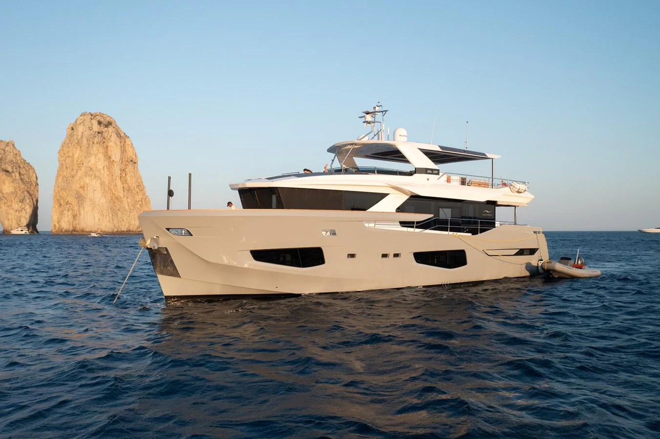 A sleek and modern yacht anchored in serene blue waters with rocky formations in the background. aboard KAMOKA Yacht for Sale